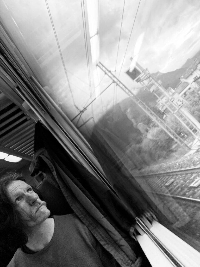 Man looking out of a train window as it speeds through the countryside.