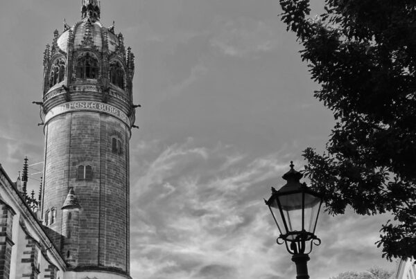 A view of the All Saints castle church tower in Lutherstadt-Wittenberg, rising high over the courtyard and the smaller buildings opposite.