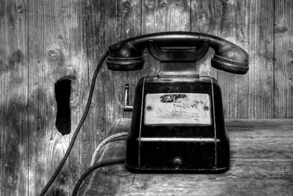 Black and white photo of an old phone with a handset resting on its horizontal cradle.