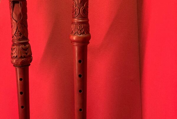 A photo of two wooden baroque recorders with intricately carved head- and foot joints and monstrous mouthpieces.
