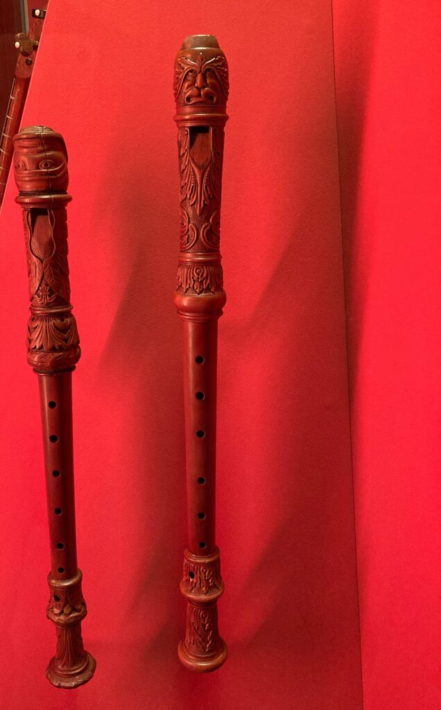 A photo of two wooden baroque recorders with intricately carved head- and foot joints and monstrous mouthpieces.