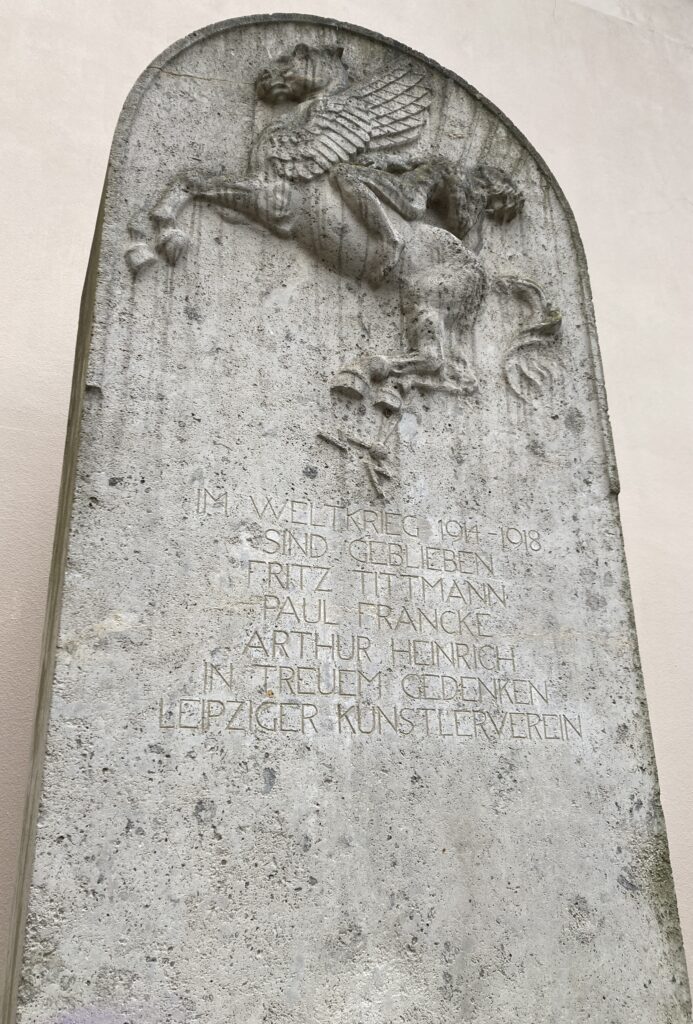 Photo depicting a stone carving of a dying man atop a Pegasus (who’s been struck by lightning) and a dedication to three artists claimed by the First World War.